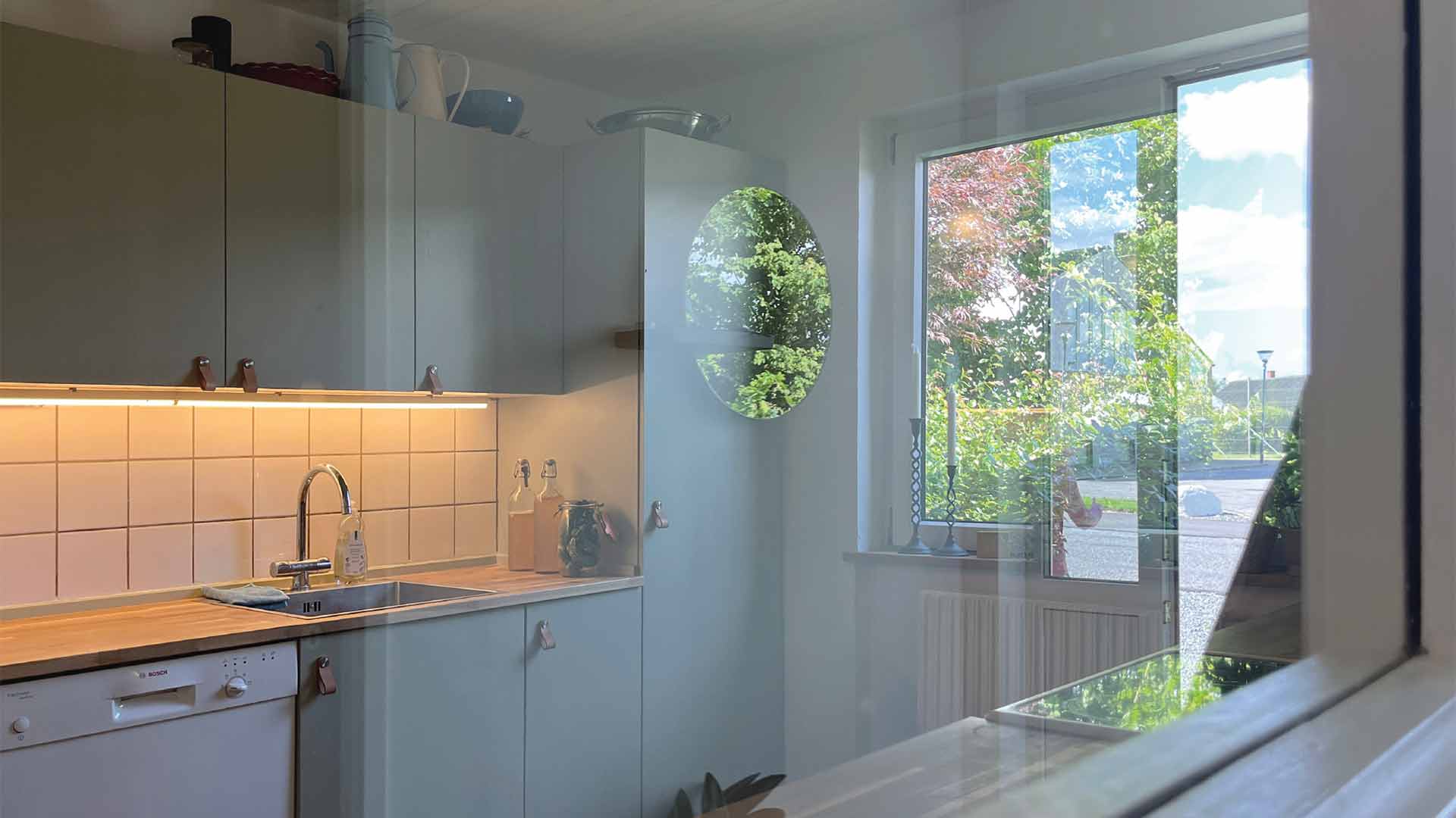 Renoveret køkken i Krejbjerg, Ginnerupvej, set fra gangen med lysindfald gennem nyt vindue. Genbrugte skabe og opdaterede fronter skaber et funktionelt og personligt køkken.
