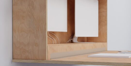 Væghængt skrivebord i birkekrydsfiner med foldbar bordplade og integreret kabelføring, monteret med fransk ophæng og udstyret med dobbelt skærme – designet af Simple Space som funktionel løsning til hjemmearbejde.